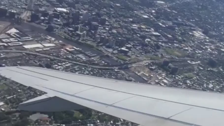 View from an airplane window: a wing above a city and winding river.